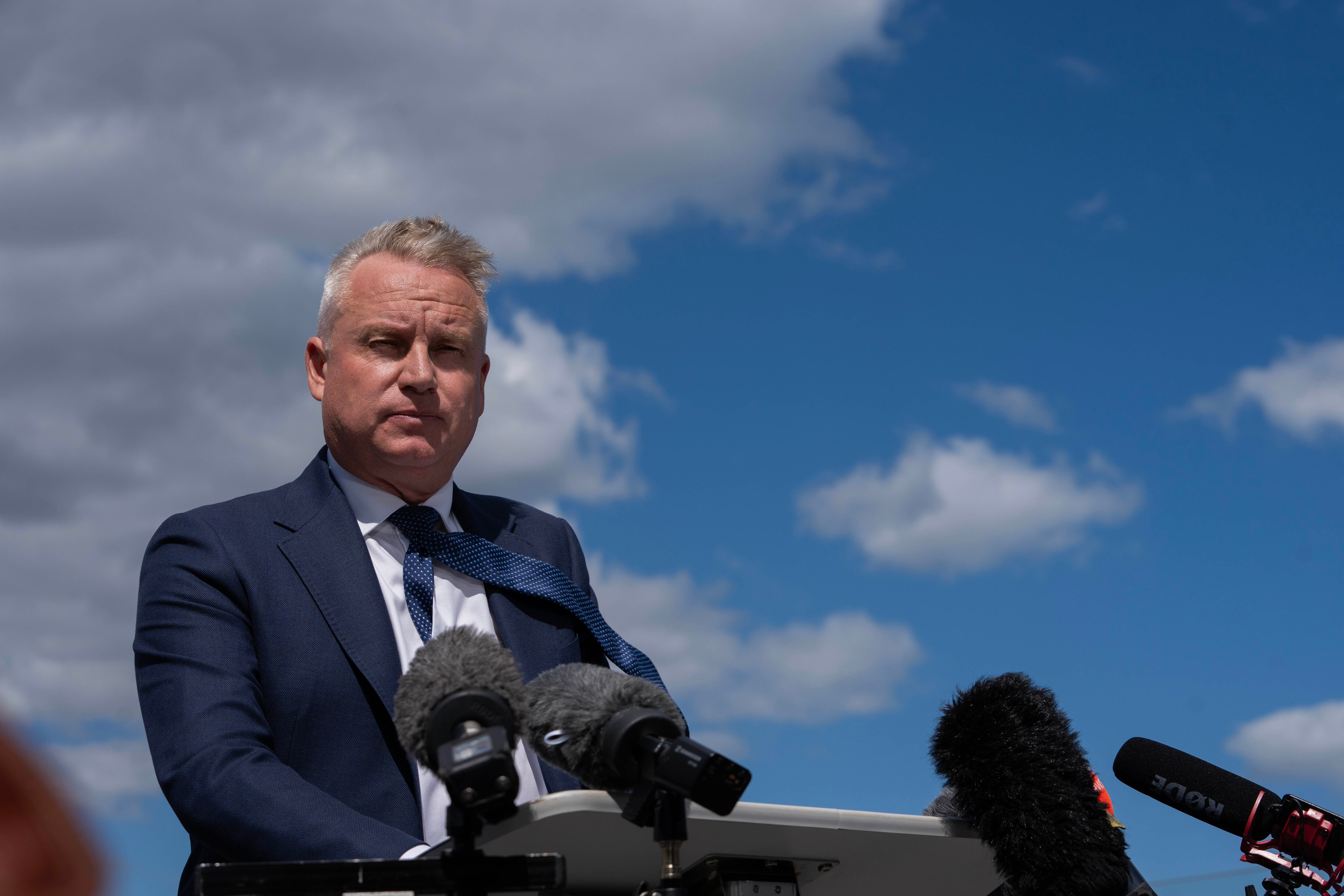 A premier speaks at a press conference on the balcony of a hotel, with the Hobart waterfront in the background.
