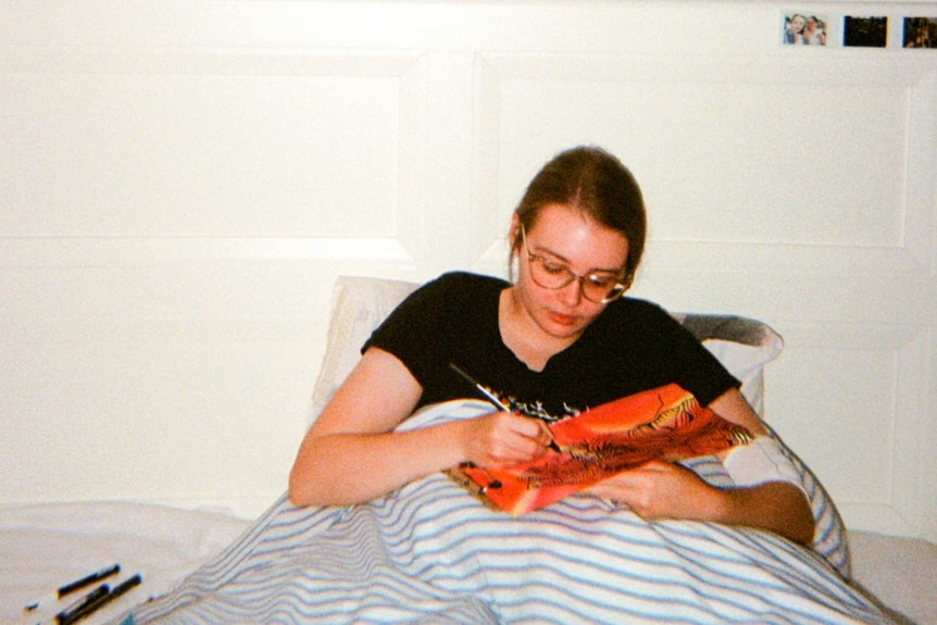 A young woman makes a painting while sitting in bed