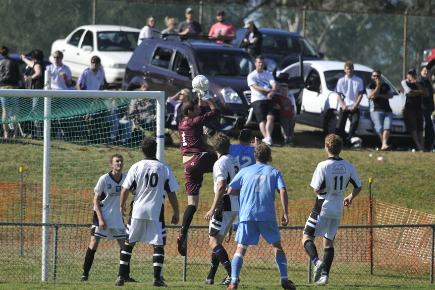 A mens soccer game, goalkeeper jumps high into air