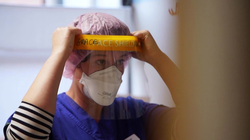 A woman wearing a mask putting a clear face shield on.