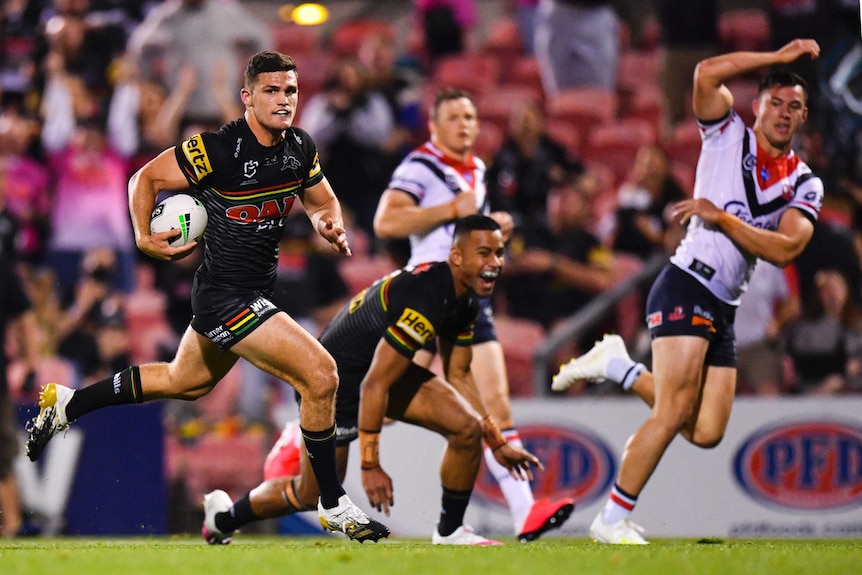 A Penrith NRL players holds the ball with his right arm as he runs towards the try line against the Roosters.