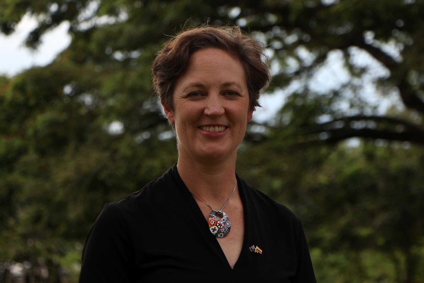 A woman smiling at the camera with trees behind her