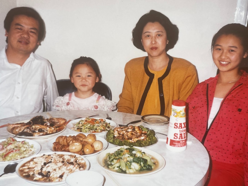 Emily Sun as a smiling child sitting with her family at a table full of food.