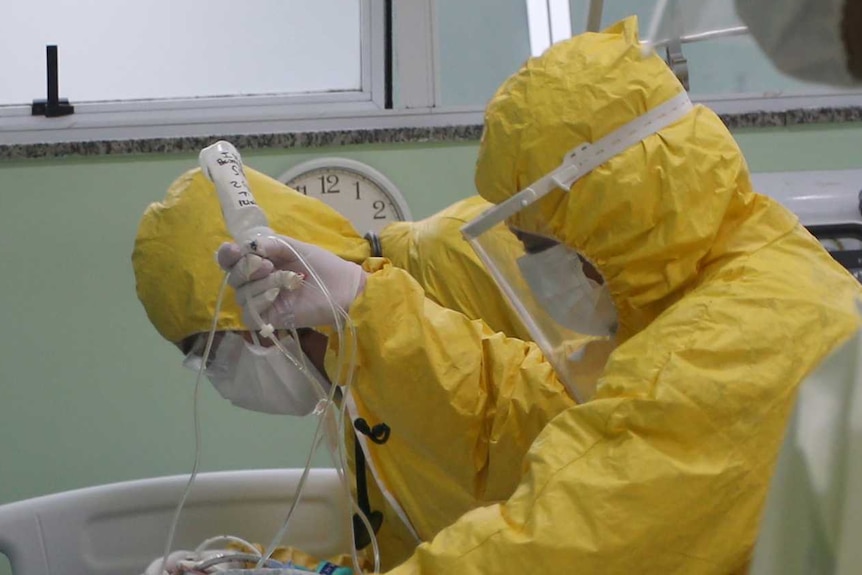 Nurses dressed in yellow protective suits bend over a patient