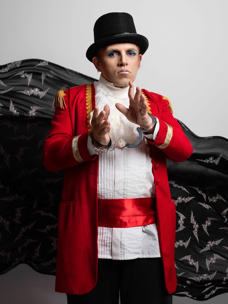 A man dressed in a red jacket, white shirt and a black hat like a top hat.