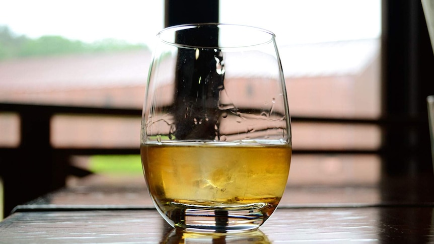 A glass of whisky sits on a table in front of a window