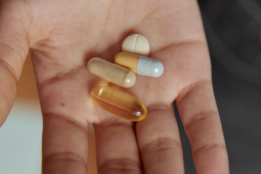 A hand holds a number of different capsules and pills.  