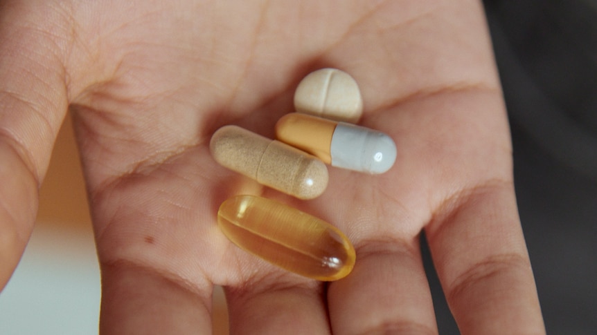 A hand holds a number of different capsules and pills.  