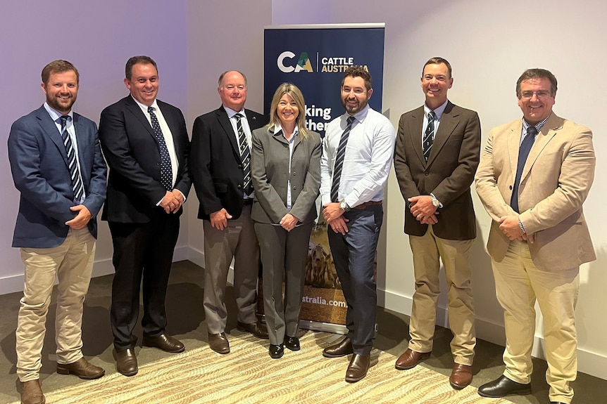 Six men and one woman in suits stand in front of Cattle Australia banner. 