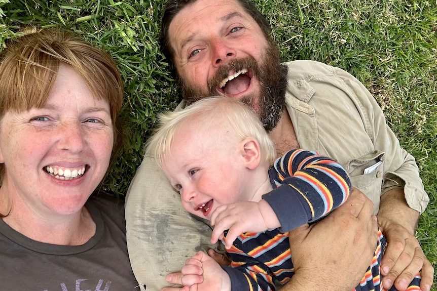 A man and woman smile with their son, lying on the ground.