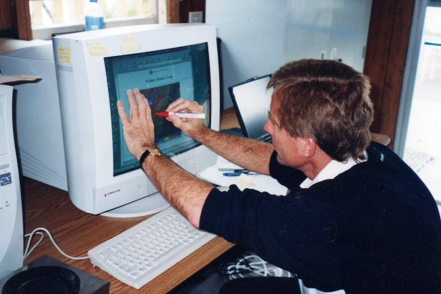 A man draws on plastic overlay over a computer screen to plot movement of rain.