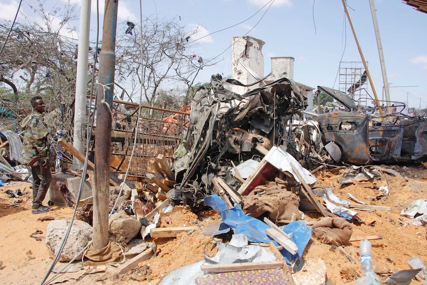 A soldier stands guard near wreckage of vehicles in Mogadishu after a car bomb.