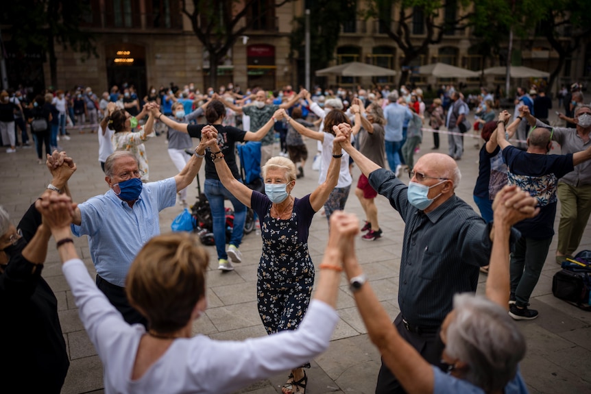 A group of people holding hands while wearing masks and dancing in a circle.