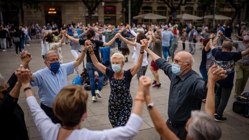 A group of people holding hands while wearing masks and dancing in a circle.