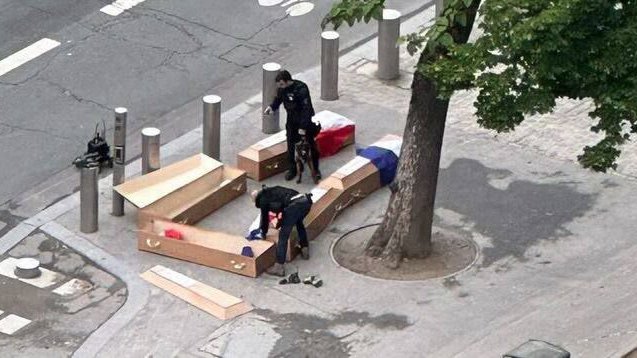 Two men assemble four coffins on a footpath while dressed in black clothes.