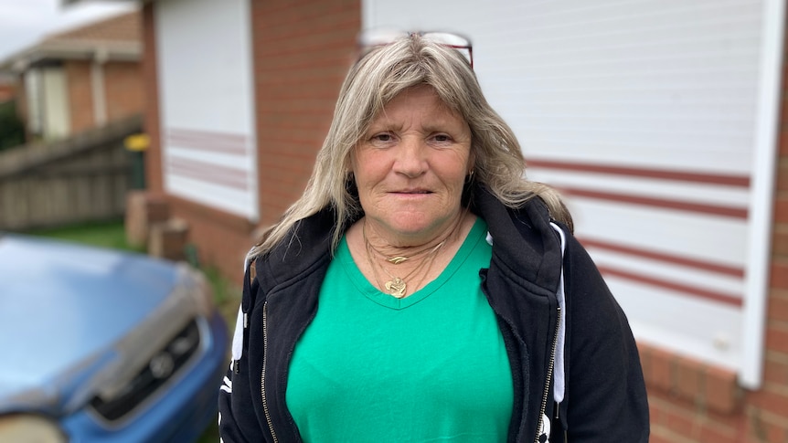 A woman in green stands in front of her home