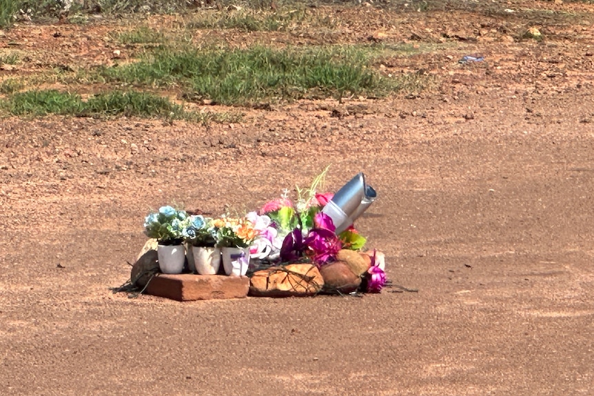 A roadside memorial with several bunches of flowers on a red dirt road.