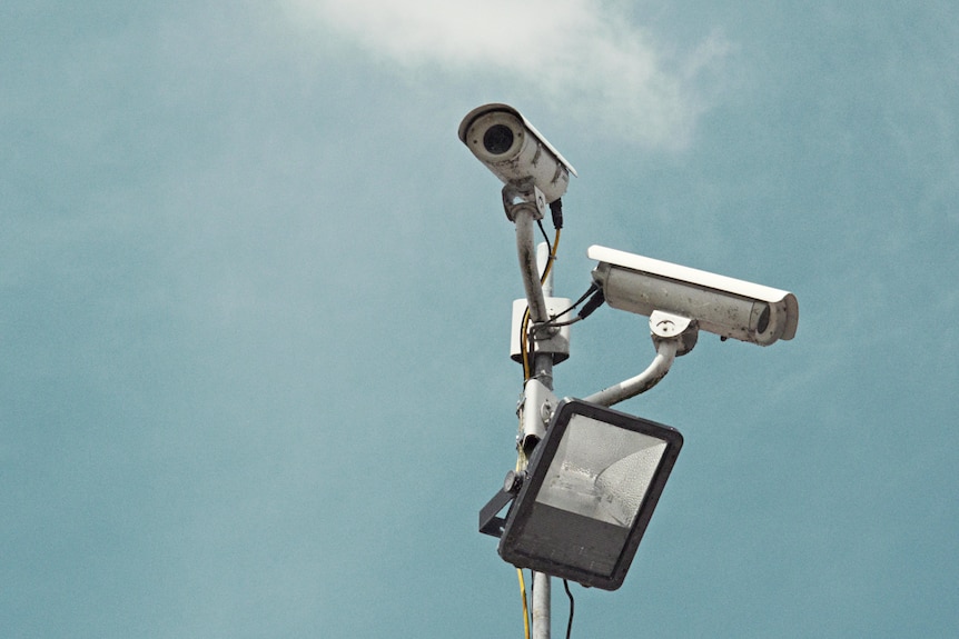 Two security cameras against a grey sky.