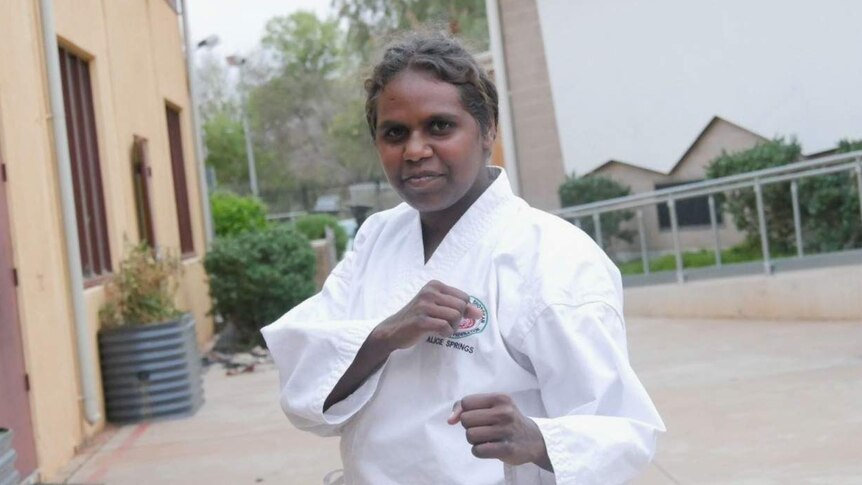 Indigenous teenager Chrissie Davis looks at the camera in karate gear, with fists raised.