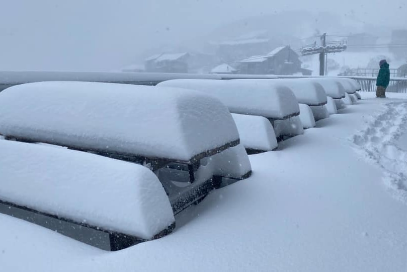 Tables covered in many centimetres of snow with a person in the background.