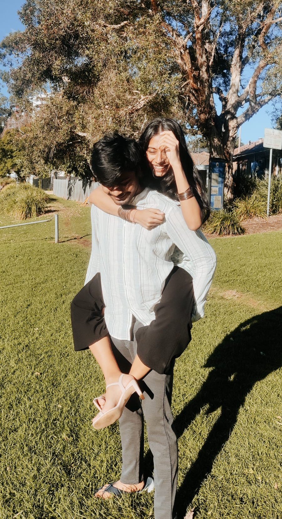 A young man in a garden gives a woman a piggyback while she smiles