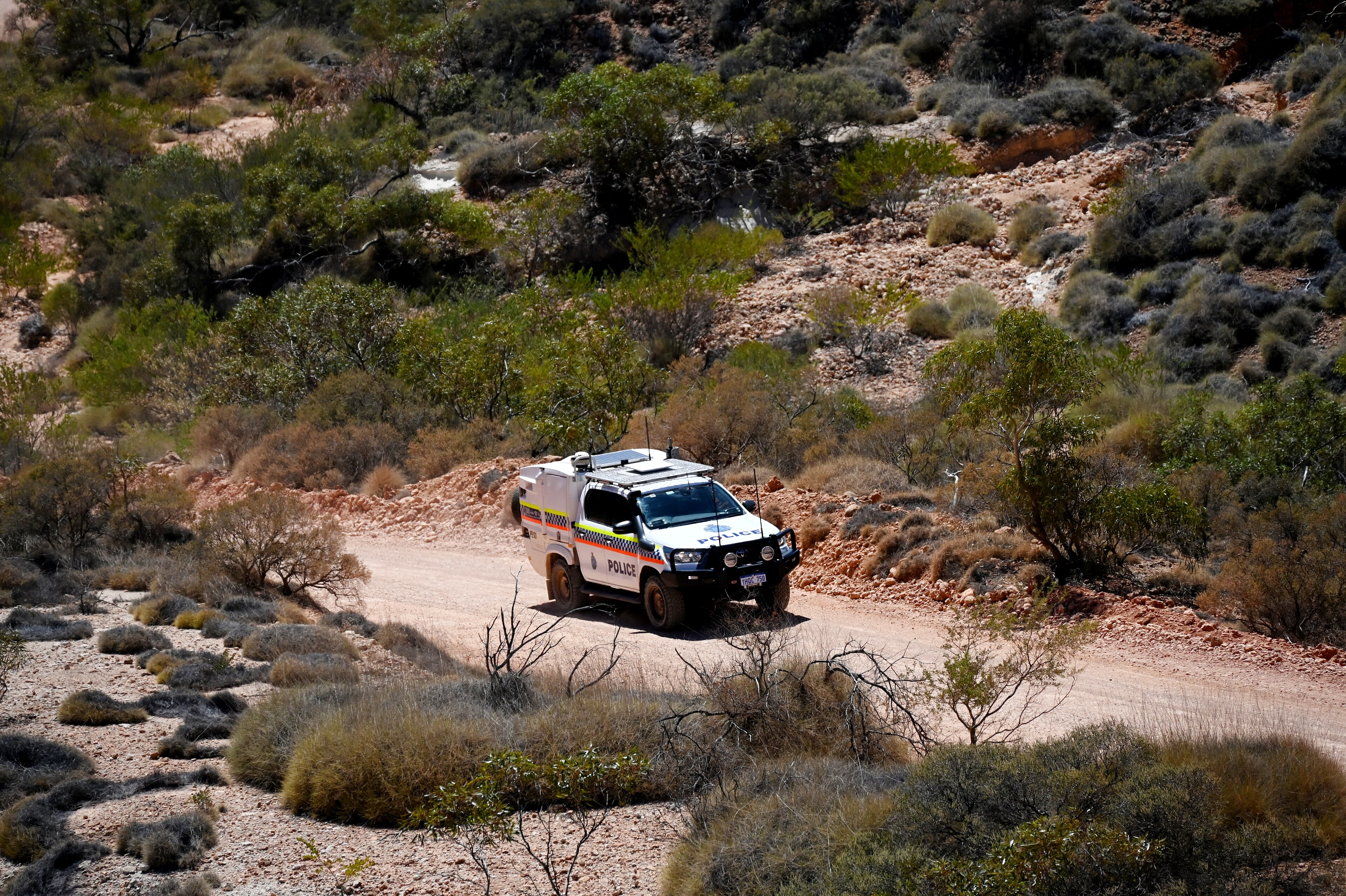 A four-wheel-drive police car on a dusty limestone track surrounded by arid scrub.