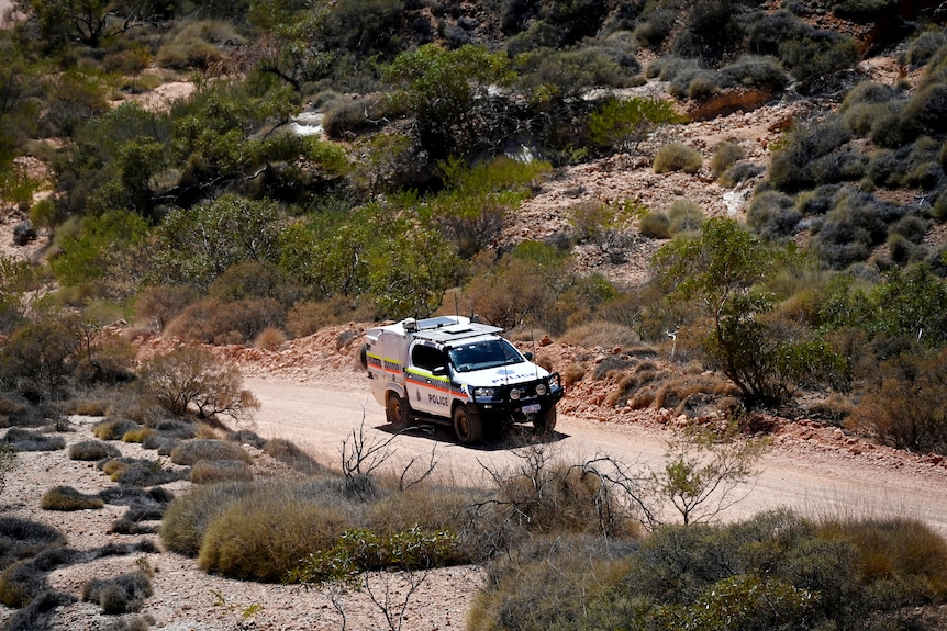 A four-wheel-drive police car on a dusty limestone track surrounded by arid scrub.