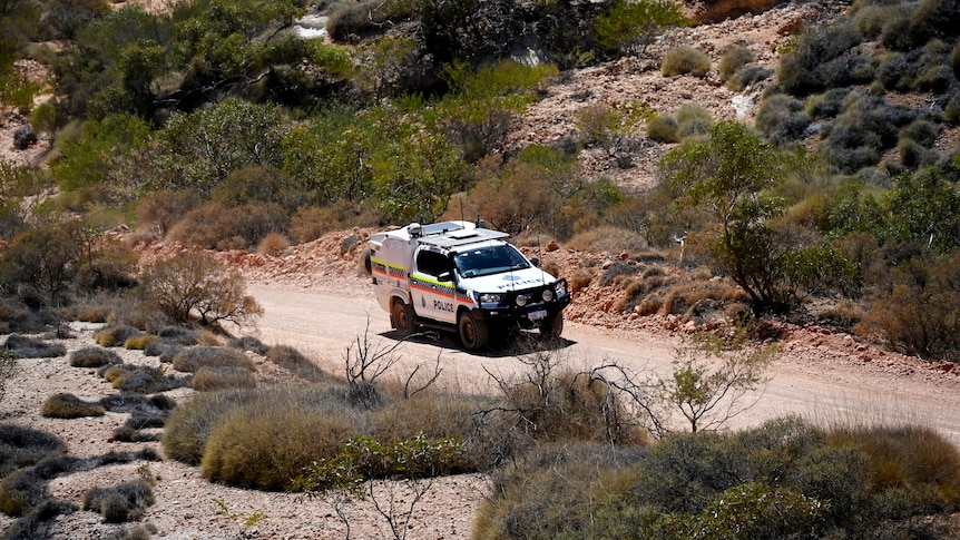 A four-wheel-drive police car on a dusty limestone track surrounded by arid scrub.