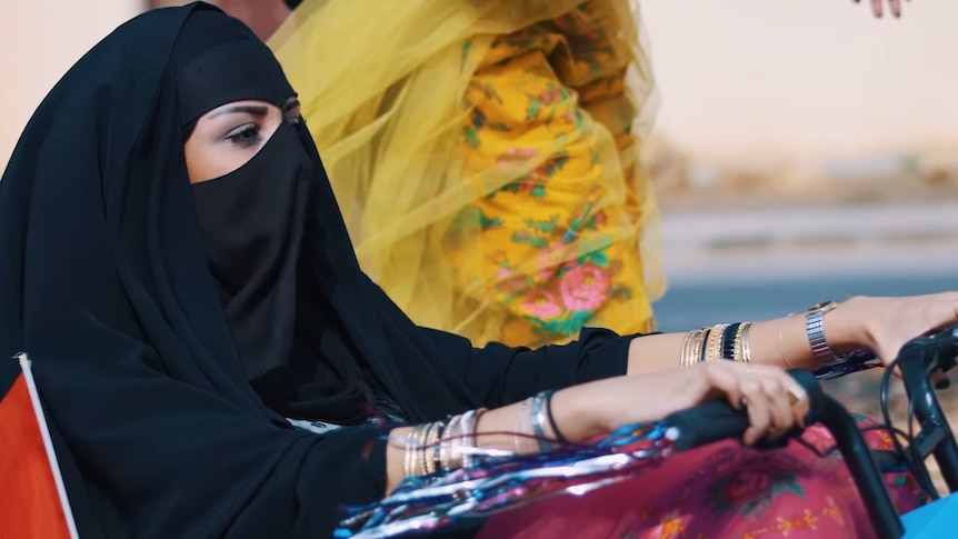 Woman wearing a niqabs rides cruiser bicycle.