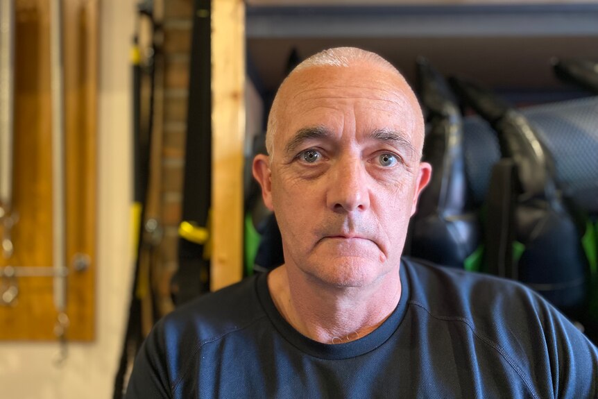 Glenn Fearnett sits in front of gym equipment and has a straight face.