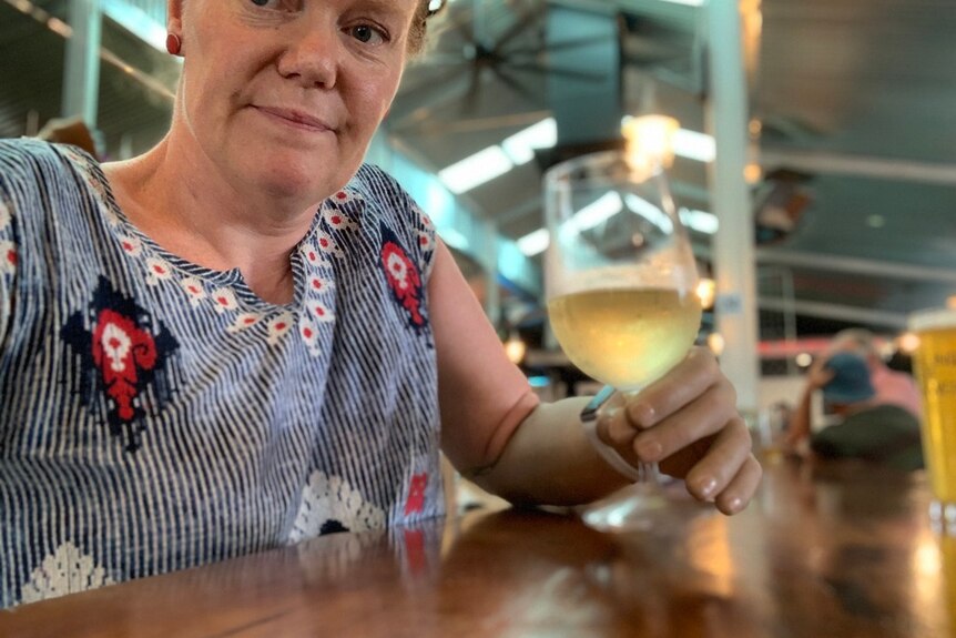 A woman takes a selfie at a restaurant as she holds a glass of white wine with her prosthetic arm.