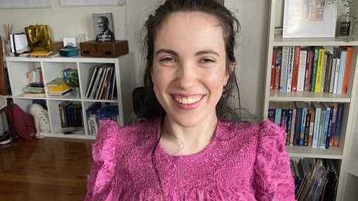 Midshot of woman with dark hair wearing a pink long-sleeve blouse, sitting in a wheelchair that is not in view.