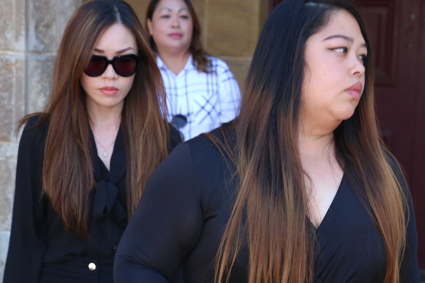 Three women dressed in black dresses, one wearing sunglasses, exit a court building.