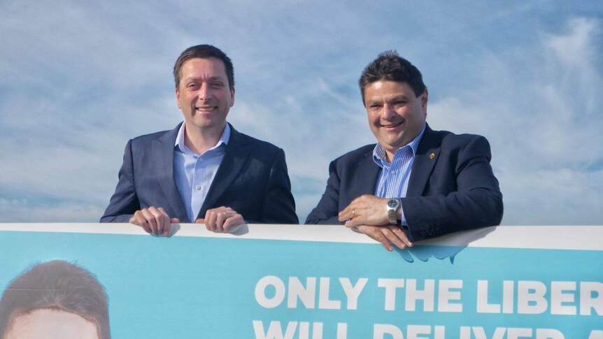The two men standing behind a large sign.