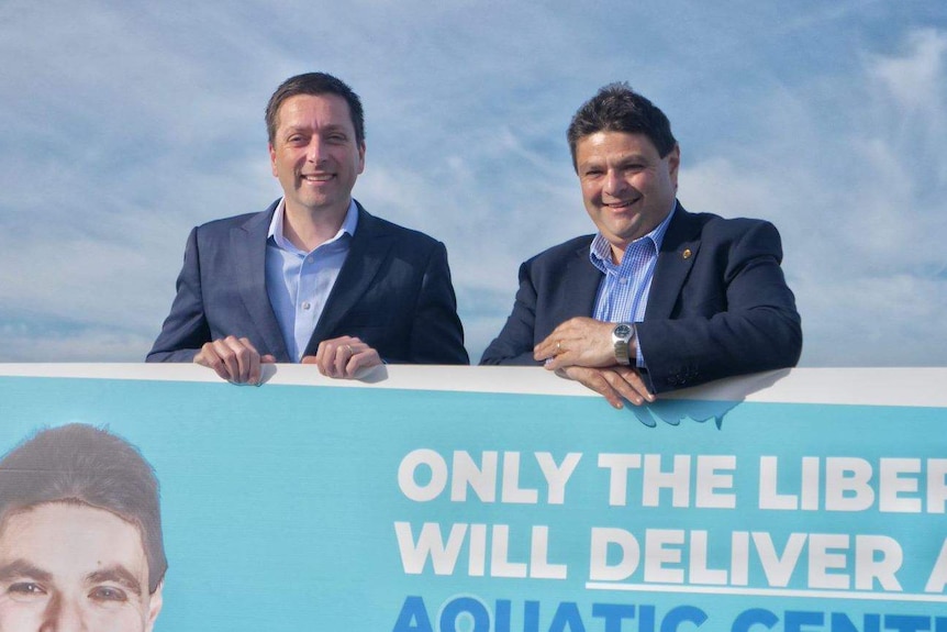 The two men standing behind a large sign.