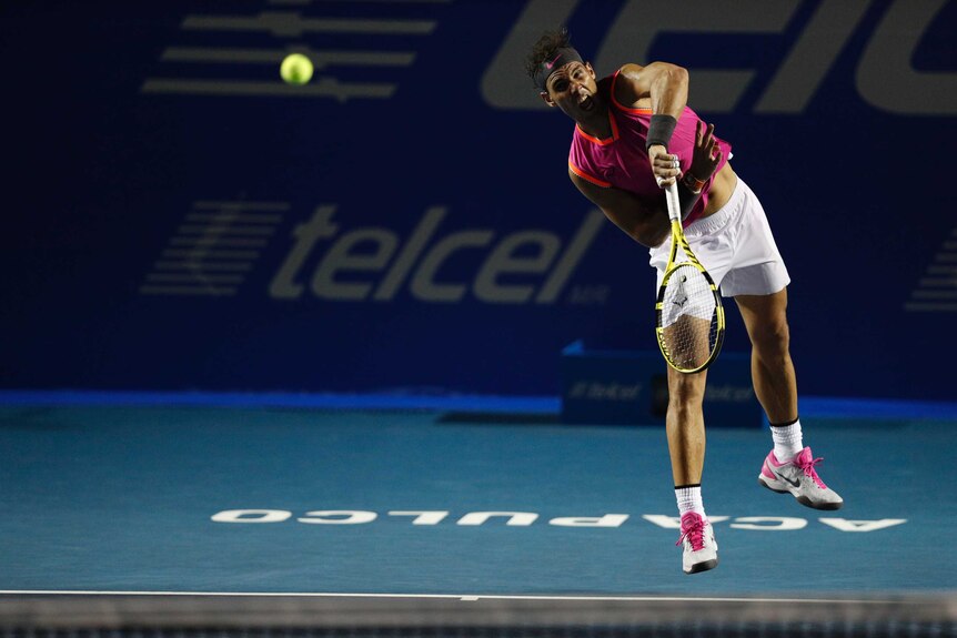 Man wearing a headband grimaces as he serves a tennis ball in a tournament in Mexico.