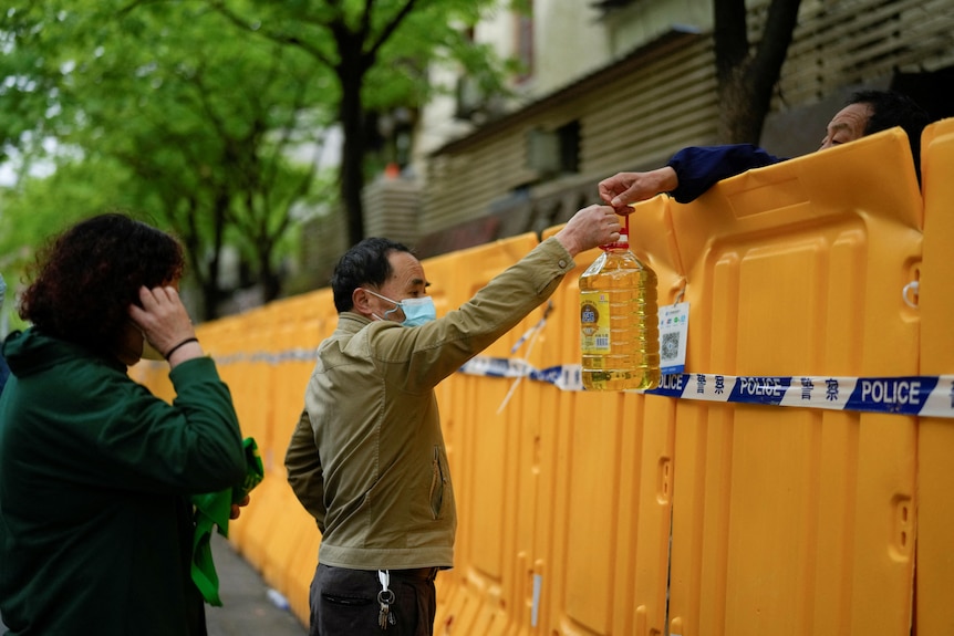 People pass edible oil over the barriers at a street market under lockdown