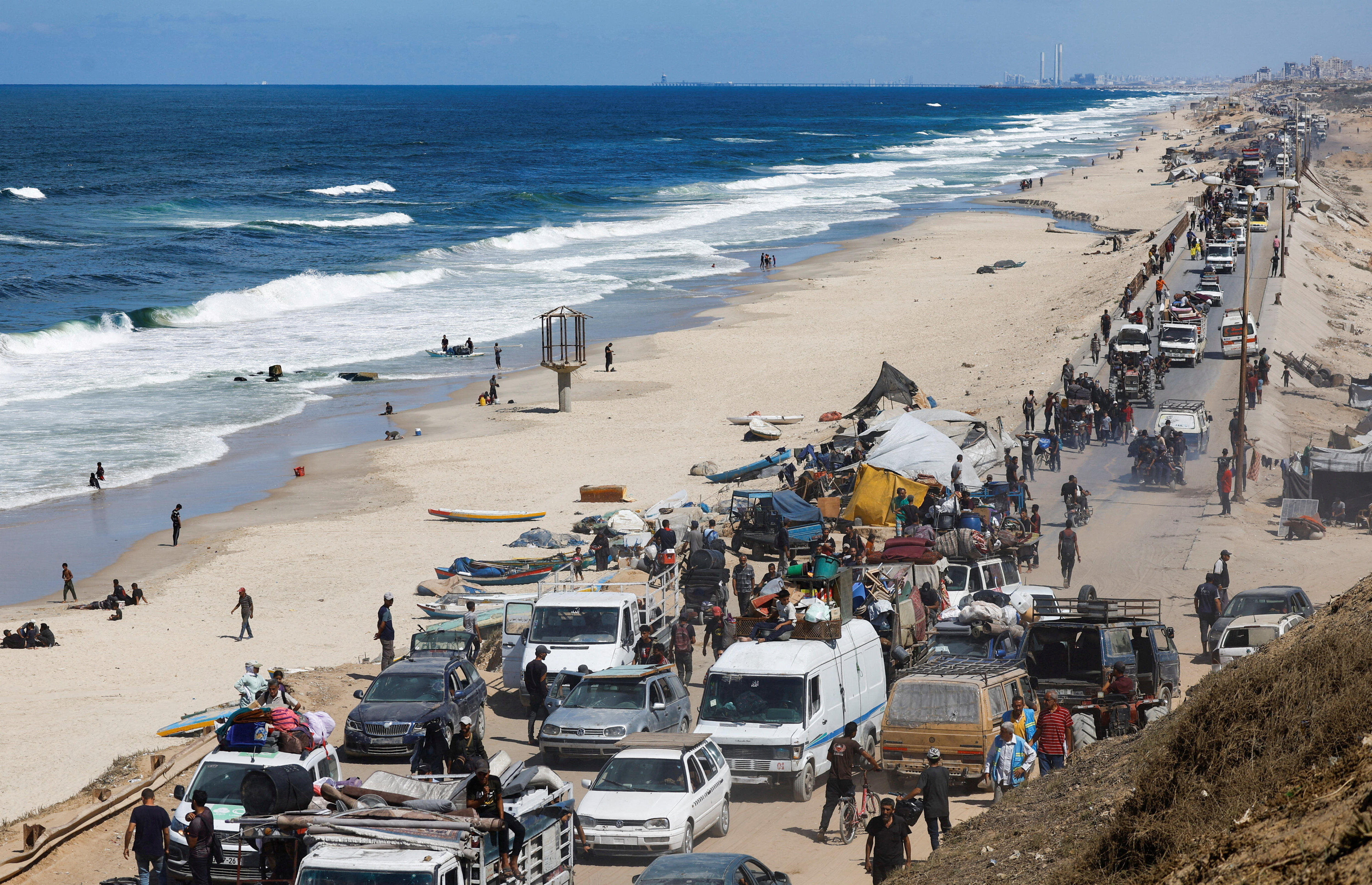 A large line of cars, vans and people streaming south along a road by the beach.