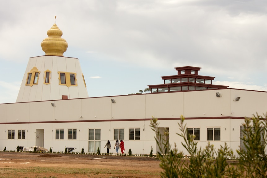 People walk past a large white building which features a golden dome.