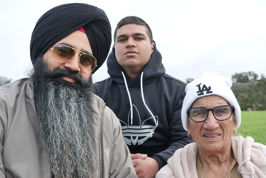 A man wearing a black turban with a boy wearing a black sweater and a woman wearing a white cap