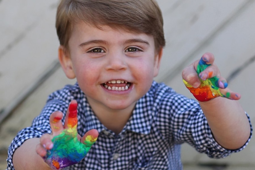 Prince Louis reaches toward the camera. The palms of his hands have been painted with rainbow colours