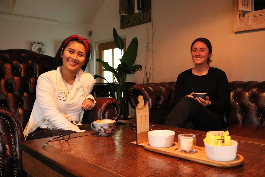 The two women sit on couches at Kita, smiling with coffees.