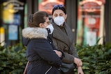 Two women walking next to each other on the street. They are wearing face masks and jackets