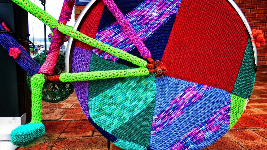 Knitted squares are attached to a wheel of a bicycle in Albany