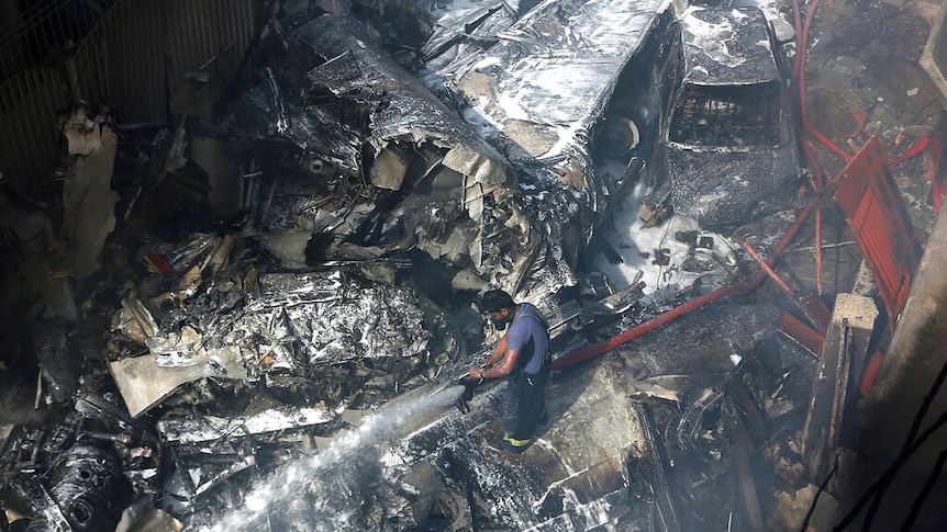 A firefighter tries to put out fire caused by plane crash, as he stands in the middle of debris.