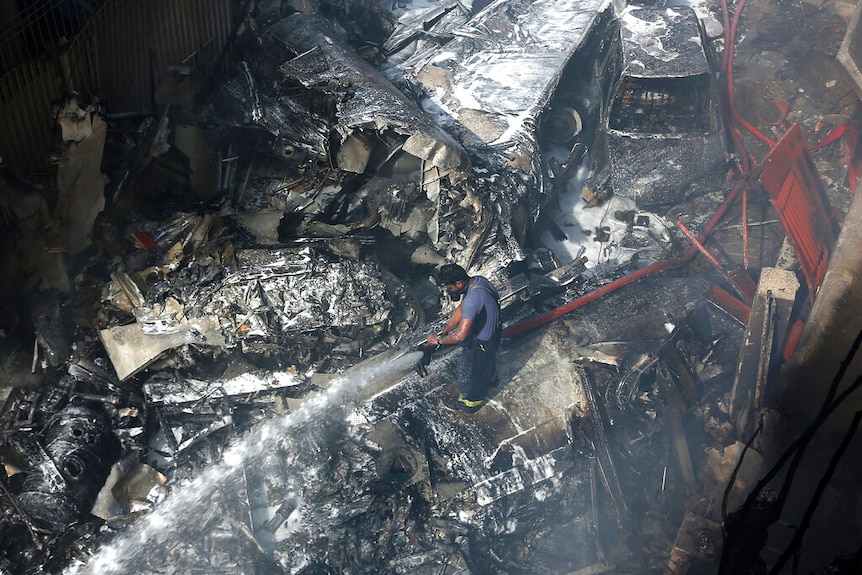 A firefighter tries to put out fire caused by plane crash, as he stands in the middle of debris.