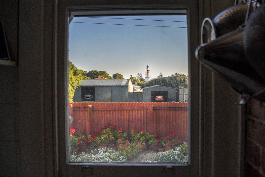 A small red and white lighthouse appears above a row of houses in the distance from a kitchen window.