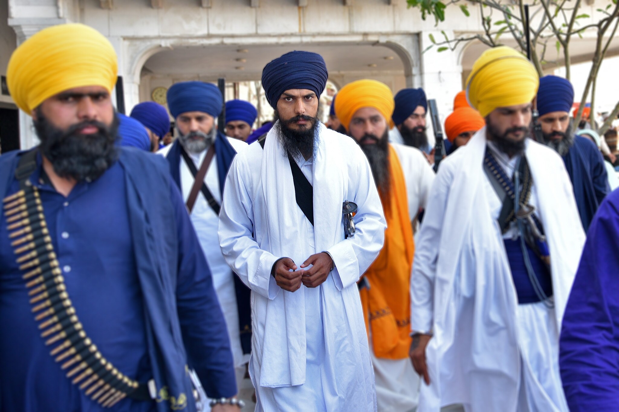 Amritpal Singh wearing white robes leaves the holy Sikh shrine of the Golden Temple with a crowd of people.
