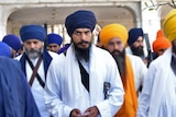 Amritpal Singh wearing white robes leaves the holy Sikh shrine of the Golden Temple with a crowd of people.