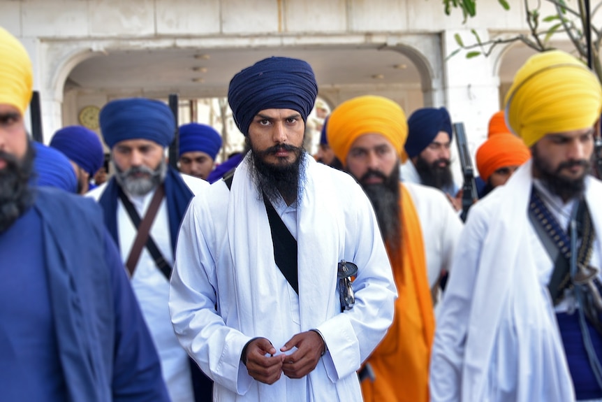 Amritpal Singh wearing white robes leaves the holy Sikh shrine of the Golden Temple with a crowd of people.